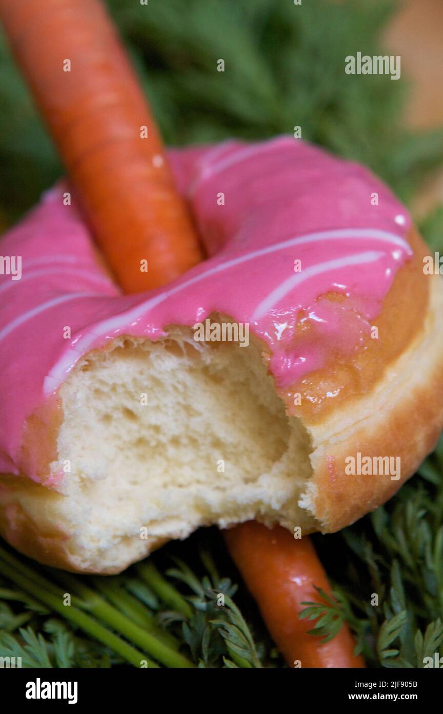 Carota fresca in ciambella rosa glassata con boccone estratto, sul letto di verde carota. Foto Stock