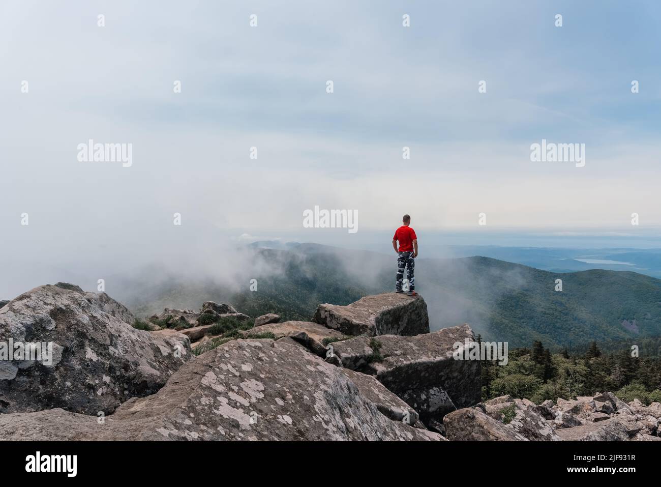 L'escursionista in cima alla montagna gode della vista aerea, sollevando le mani sopra le nuvole. Monte Pidan. Foto di alta qualità Foto Stock