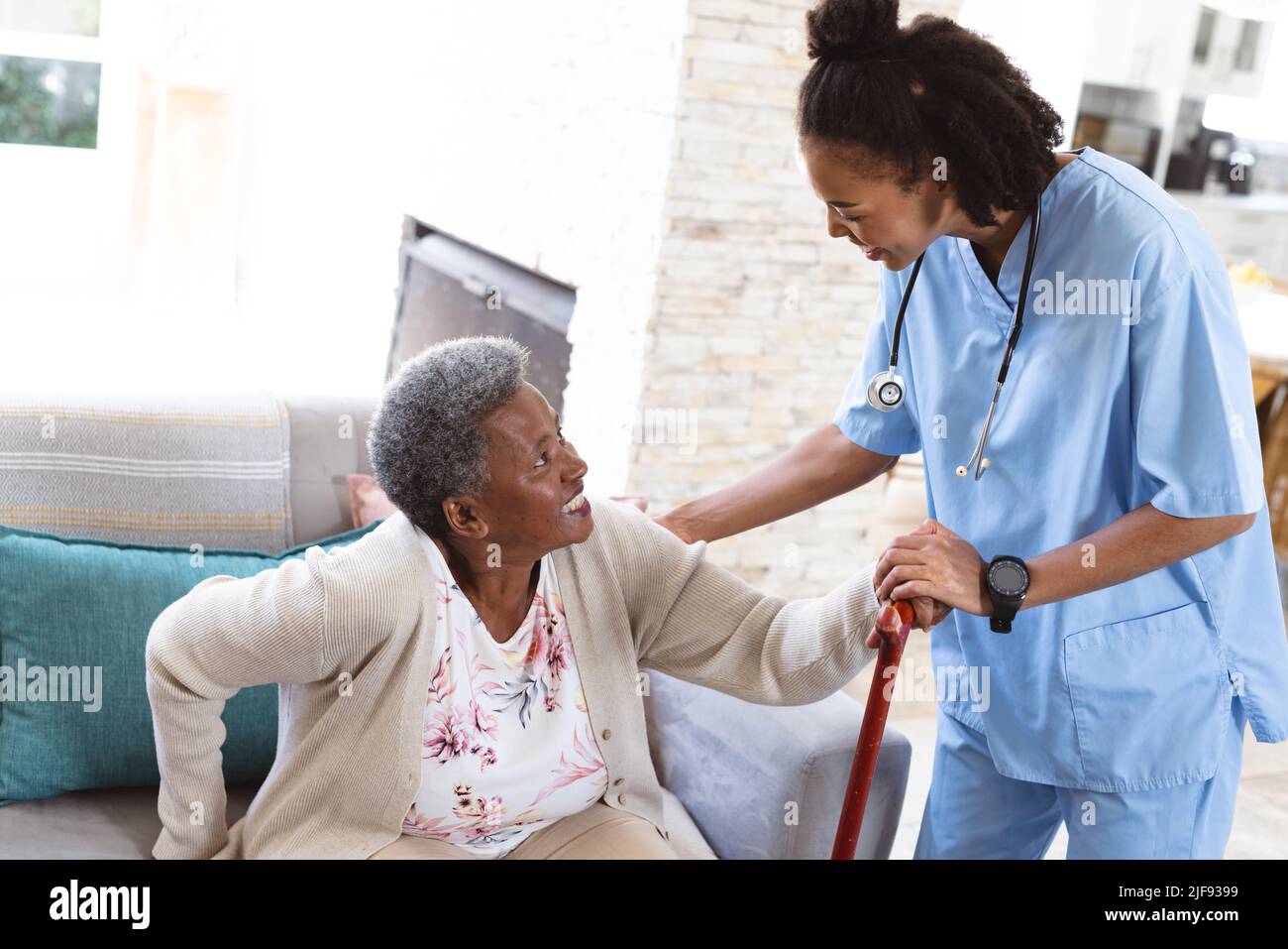 Donna africana americana anziana che tiene bastone camminare alzarsi con l'aiuto di medico femminile a casa Foto Stock