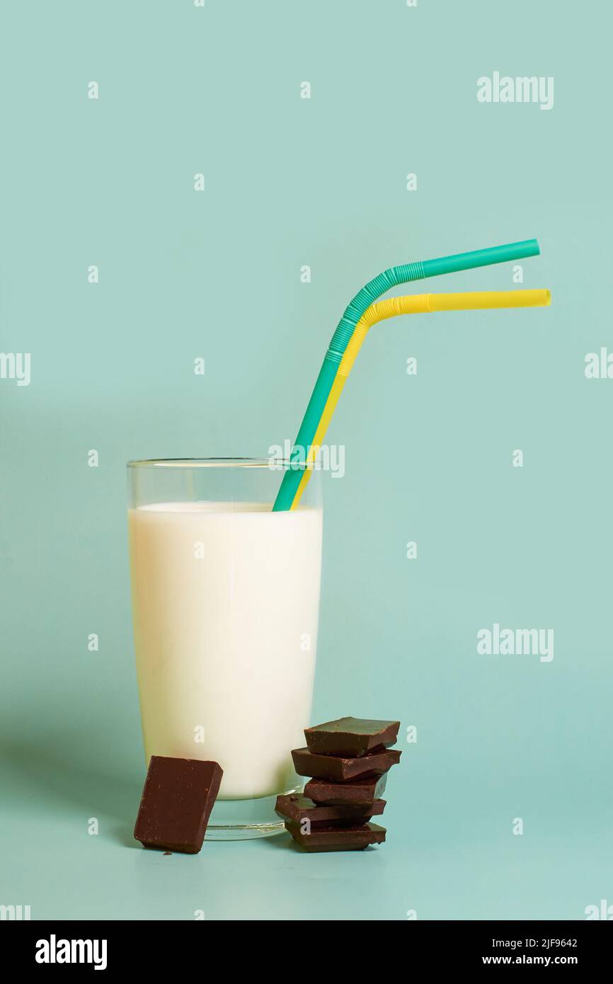 Un bicchiere di latte, due tubi di plastica e pezzi di cioccolato fondente Foto Stock