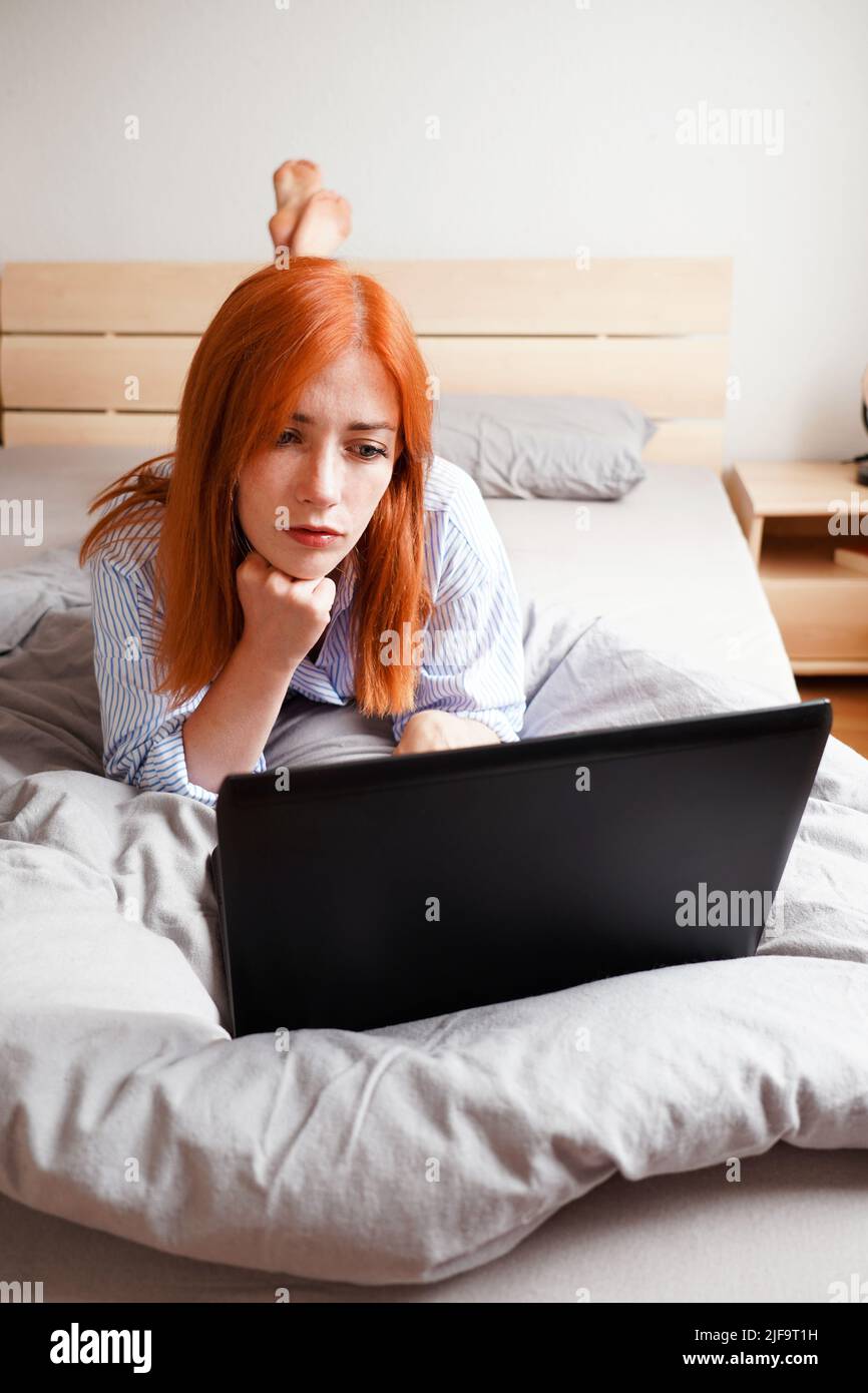 Giovane donna sdraiata sul letto con il computer portatile Foto Stock