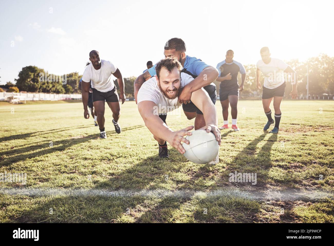 Giocatore di rugby caucasico che si tuffa per segnare una prova durante una partita di rugby fuori su un campo. Giovane atleta maschile che fa un tuffo per provare a vincere il gioco per suo Foto Stock