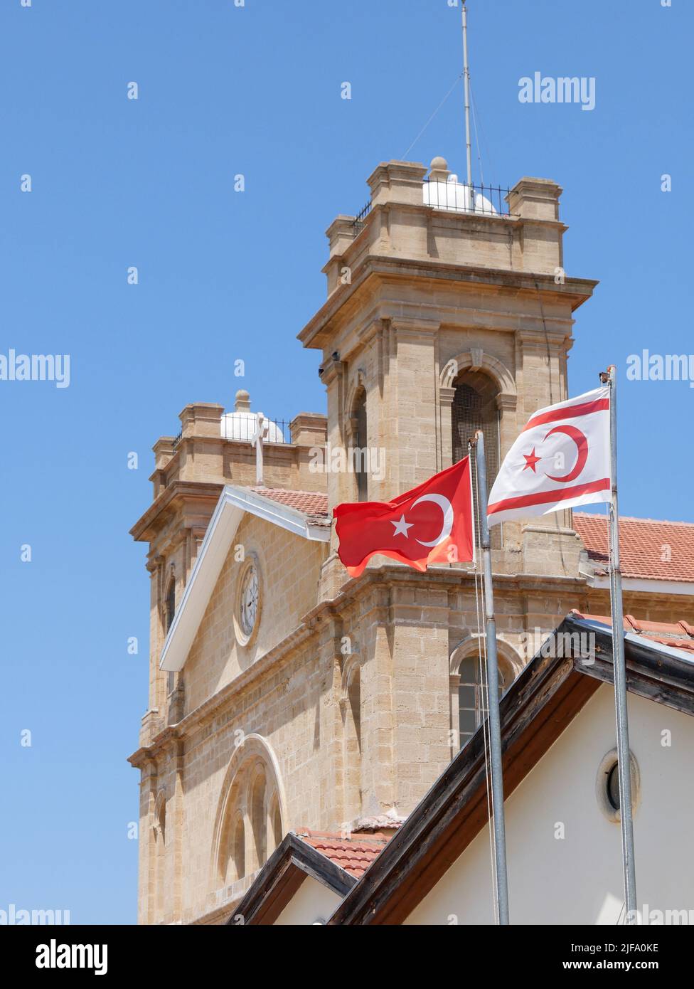 Cattedrale di San Giorgio, uno degli ultimi villaggi maroniti cristiani di Cipro del Nord con una bandiera turca e cipriota del Nord che vola oltre ad essa Foto Stock