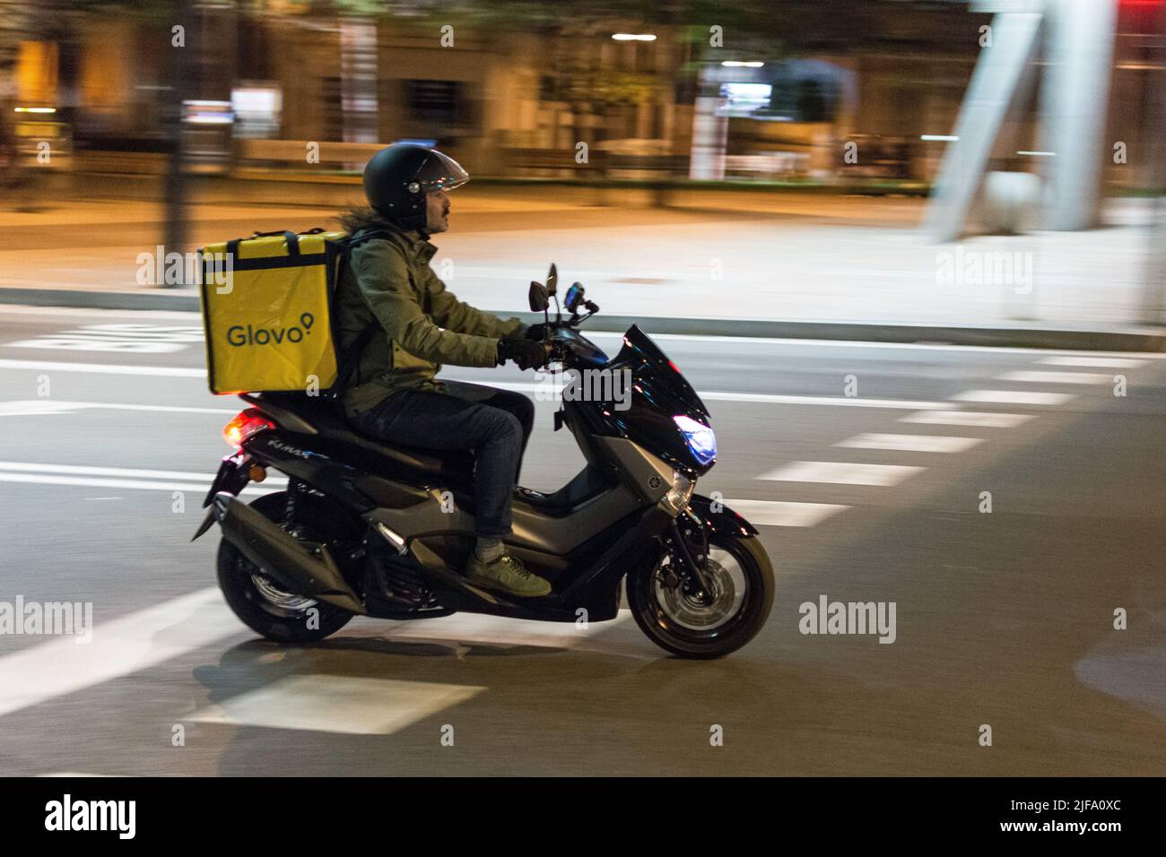 Uomo di consegna con scooter in città di notte. Yamaha Nmax Glovo Foto Stock