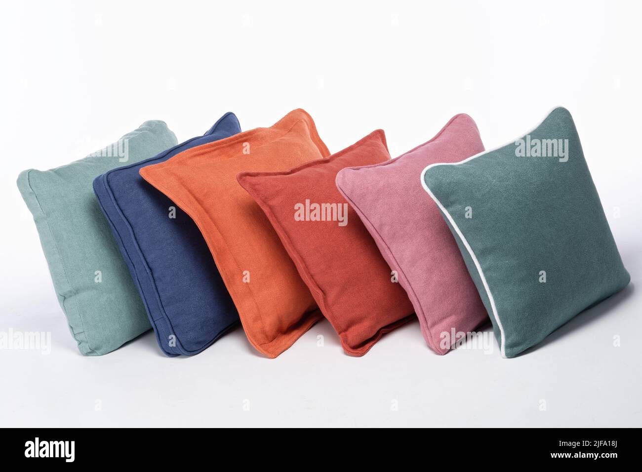 Sei diversi cuscini che si appoggiano l'uno contro l'altro su sfondo bianco. Un arcobaleno di colori e stili di cuscini per divani. Foto Stock