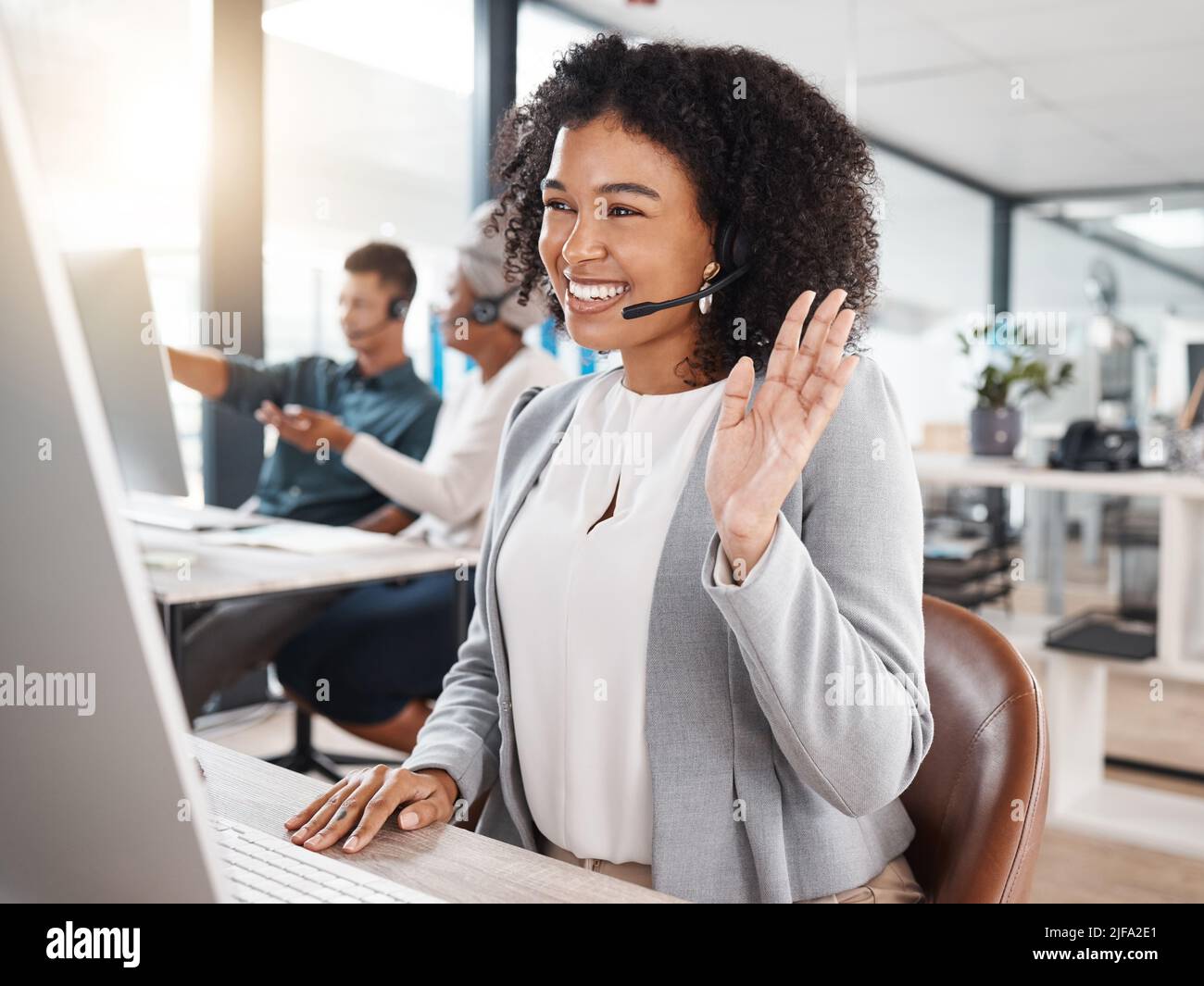 Felice agente di telemarketing misto del call center di gara che salutano durante una riunione virtuale tramite videochiamata su un computer in ufficio. Consulente femminile Foto Stock