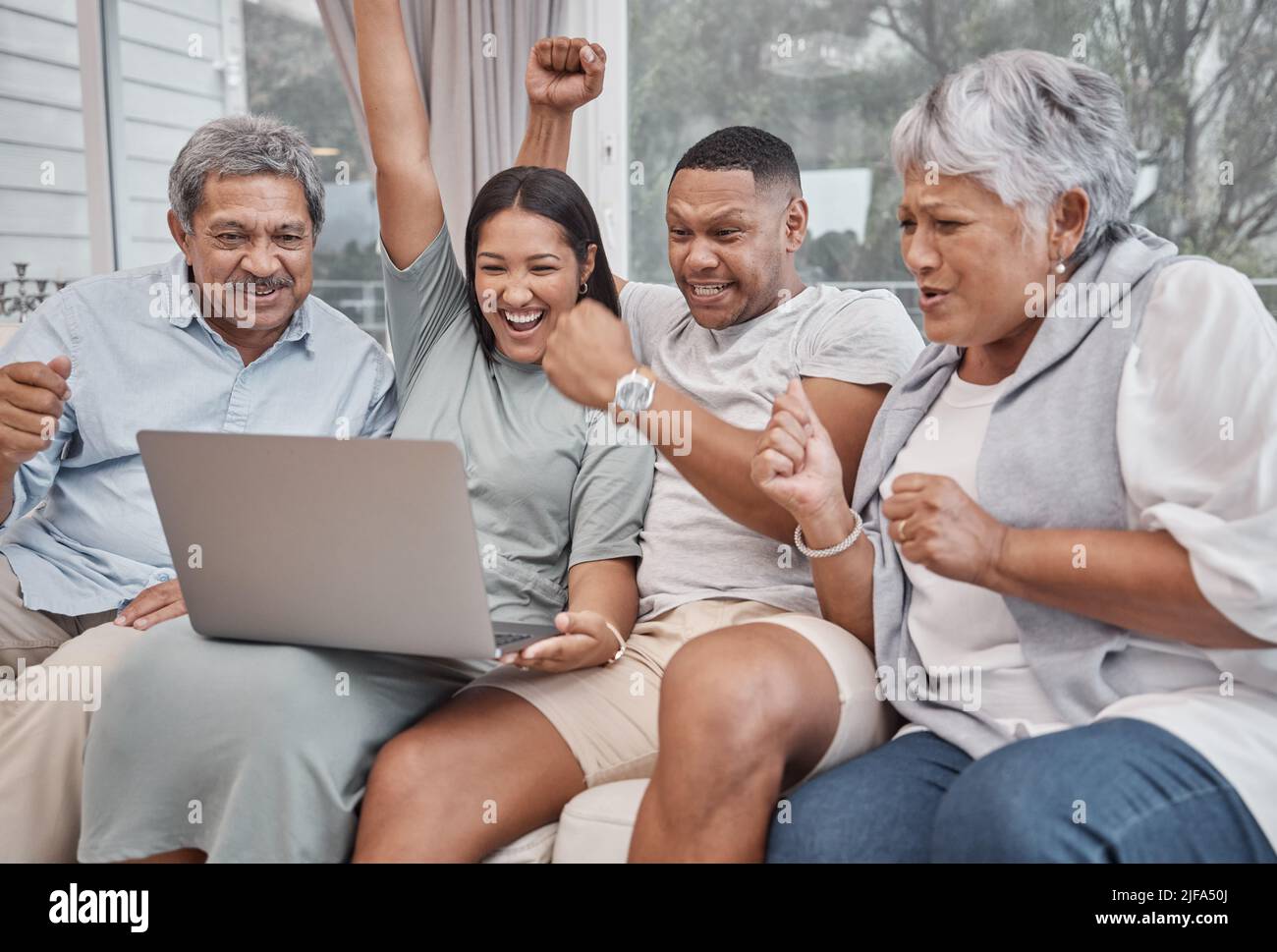 Una famiglia di quattro persone allegra e affettuosa che si occupa di gare miste e utilizza un computer portatile per guardare gli sport e per allietare la propria squadra preferita nel salotto di casa. Sposato Foto Stock