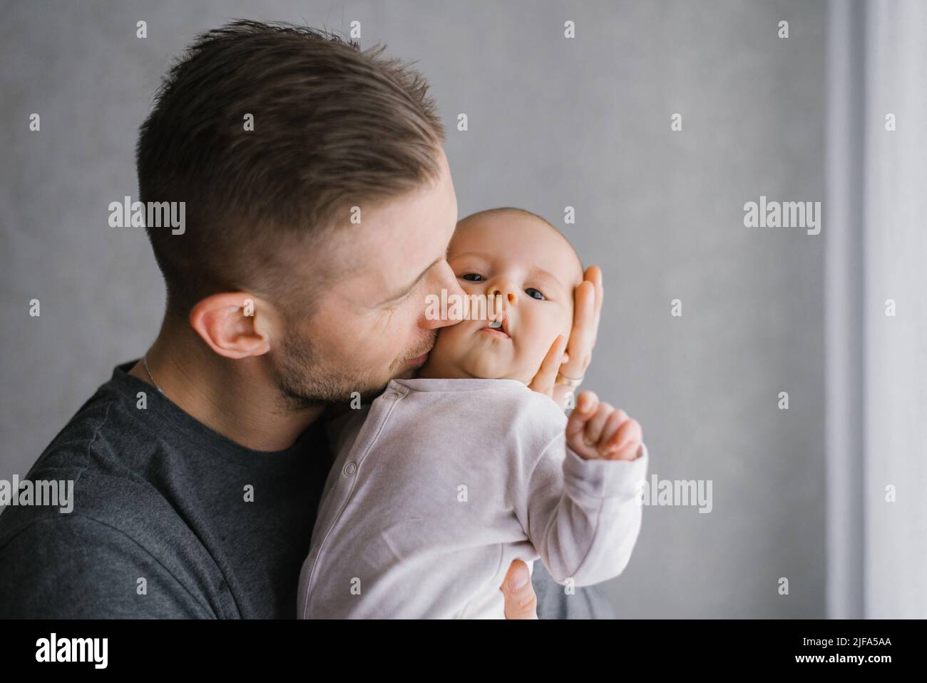 Papà tiene il bambino tra le braccia a casa e bacia il bambino sulla guancia Foto Stock