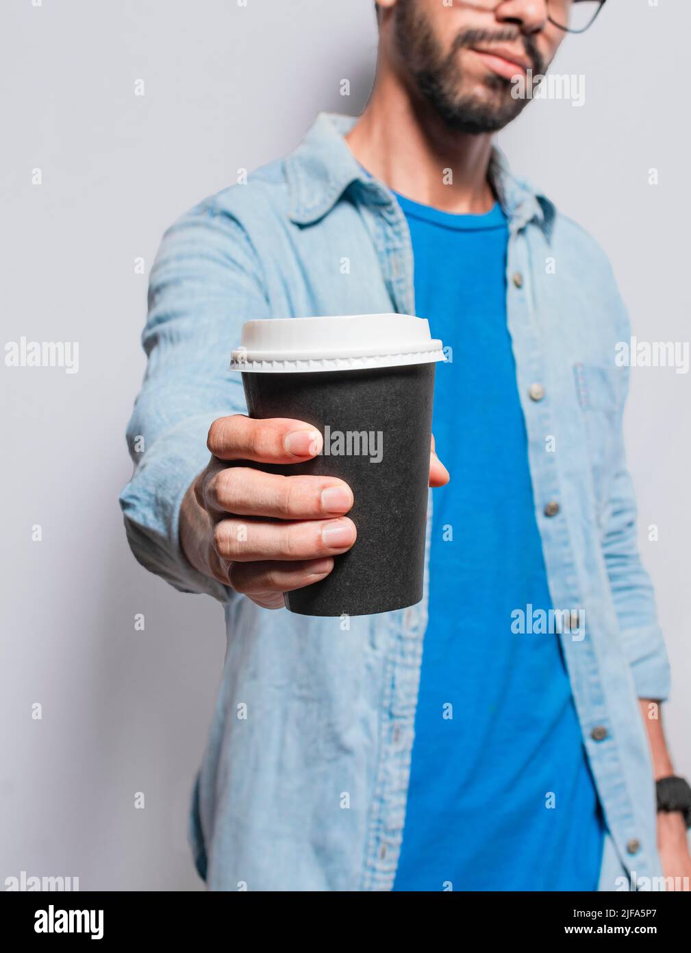 Primo piano di persona che offre un caffè da andare, giovane uomo che offre alla macchina fotografica un caffè da andare, bel uomo che tiene un caffè per andare isolato Foto Stock