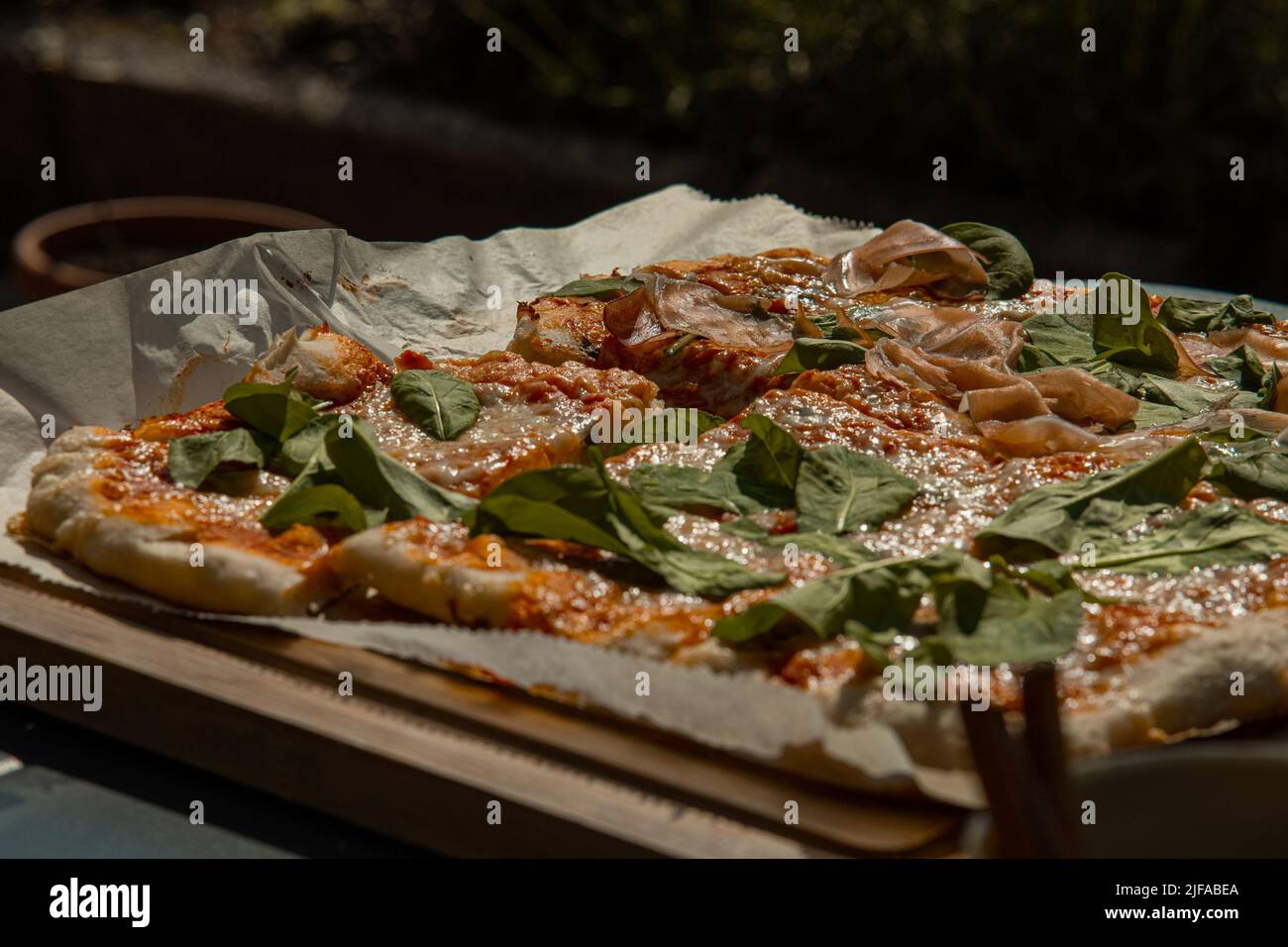 Deliziosa pizza fresca fatta in casa servita su un asse di legno e un po' di carta. Pizza gustosa pronta per essere tagliata. Foto Stock