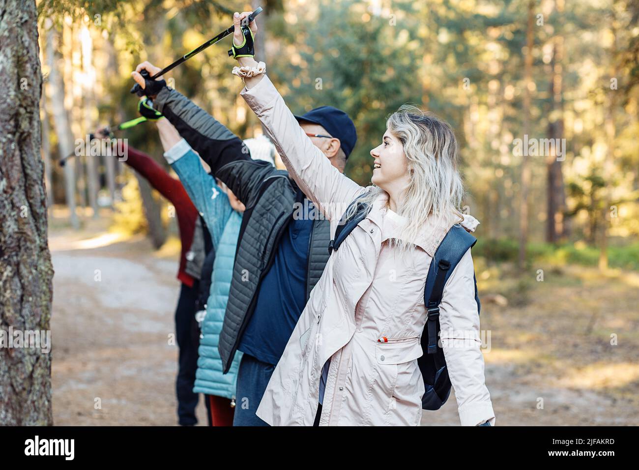 Gruppo di persone che tengono in aria i bastoni da trekking nordici durante il trekking nella foresta, guardando verso l'alto. Formazione all'attività Foto Stock