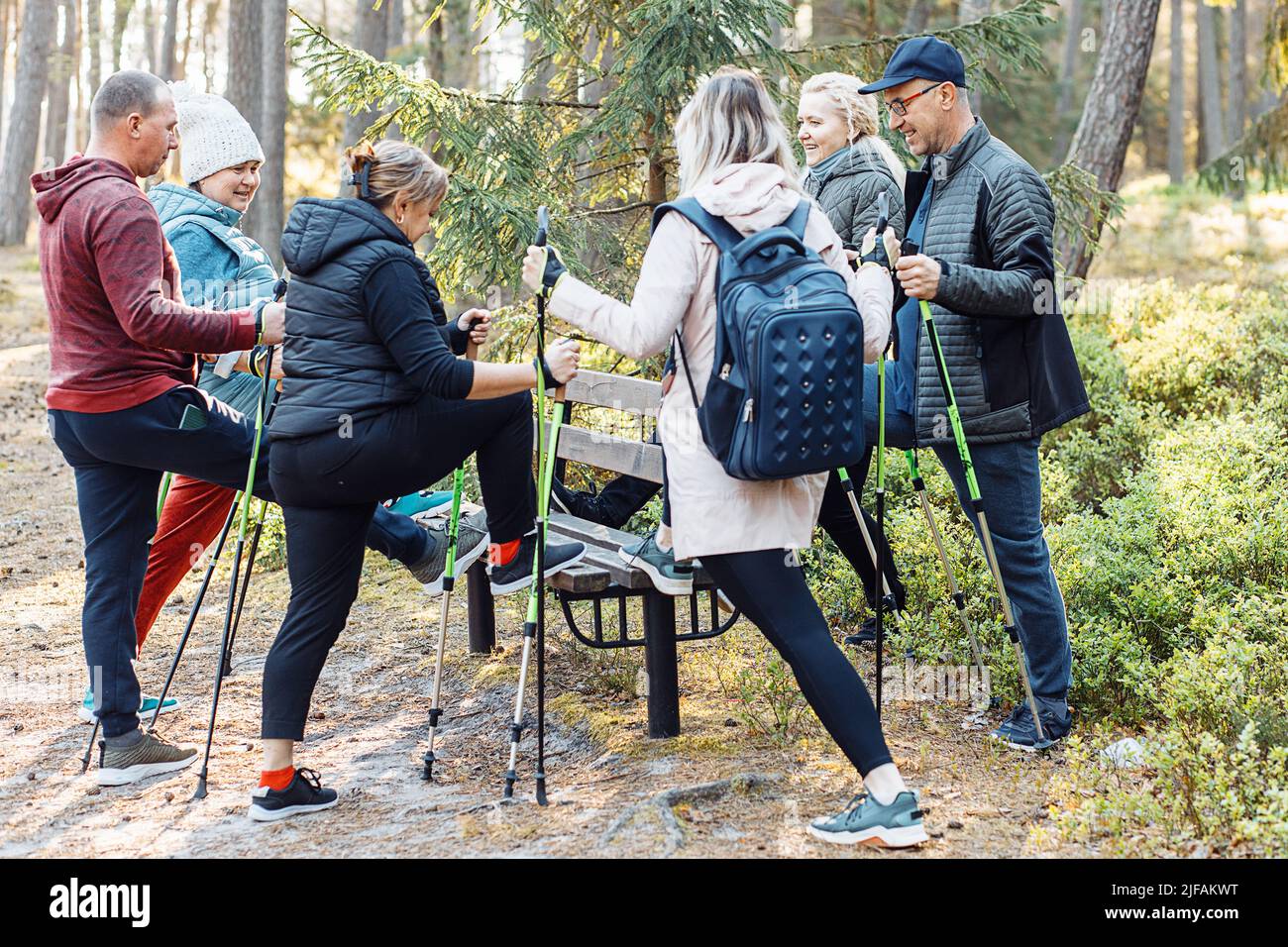 Gruppo di persone anziane che imparano a fare nordic walking con bastone da trekking nella foresta, si levano in piedi una gamba sulla panca. Esercitandosi Foto Stock