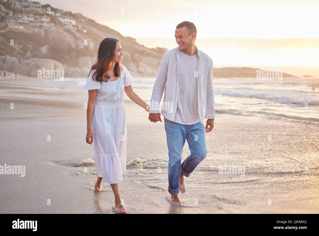 Affettuoso misto coppia corsa tenendo le mani e camminando lungo la spiaggia. Marito e moglie si mano nella sabbia accanto al mare. Godendo di un romantico Foto Stock