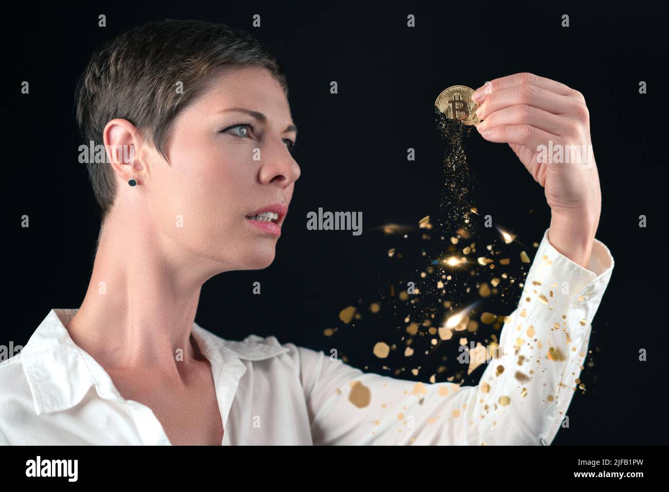 Attraente donna business con capelli corti in camicia bianca che tiene bitcoin d'oro disperdendo in polvere scintillante. Concetto di crisi del bitcoin, svalutazione, Foto Stock