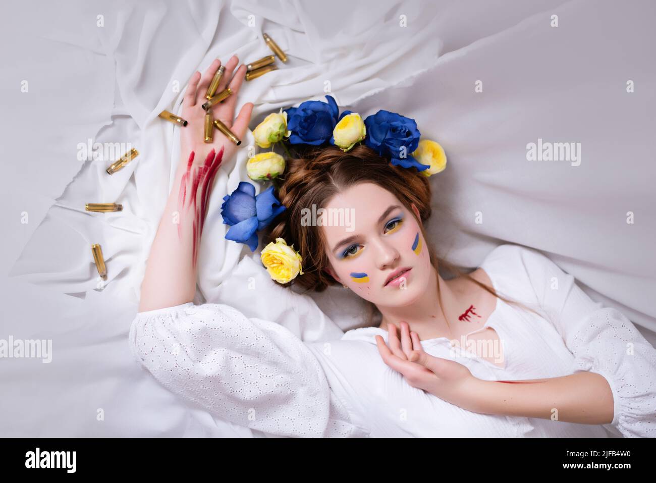 Una giovane donna Ucraina durante la guerra con una corona blu gialla di proiettili e sangue su sfondo bianco da vicino. La Russia ha attaccato l'Ucraina nel 2022 Foto Stock