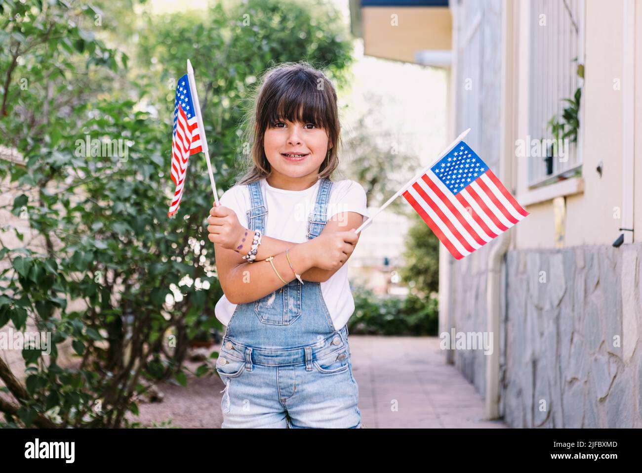 Piccola ragazza dai capelli neri con bandiere americane nel giardino della sua casa. Concetto di celebrazione, giorno d'indipendenza, 4th luglio, patriottismo, vacanza e Foto Stock