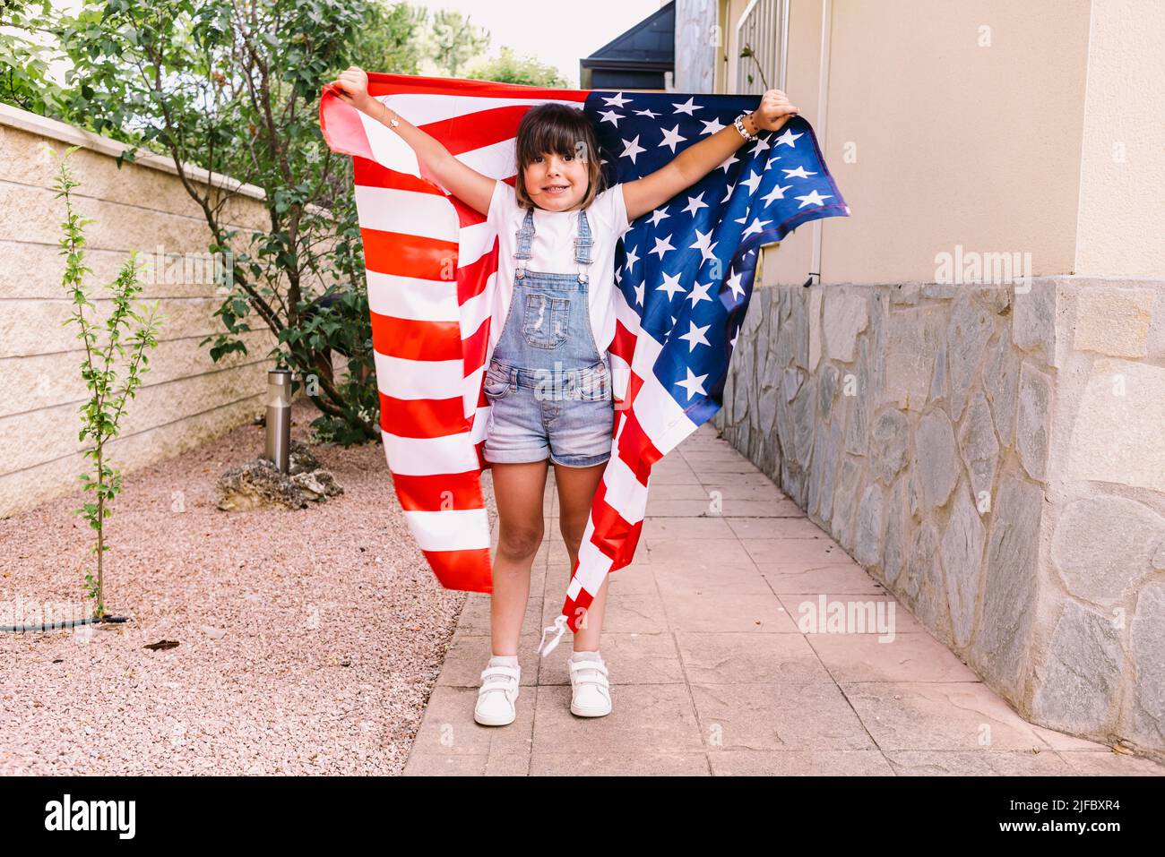 Ragazza dai capelli neri coperta da una grande bandiera americana, nel giardino della sua casa. Concetto di celebrazione, giorno di indipendenza, Stati Uniti d'America, Foto Stock