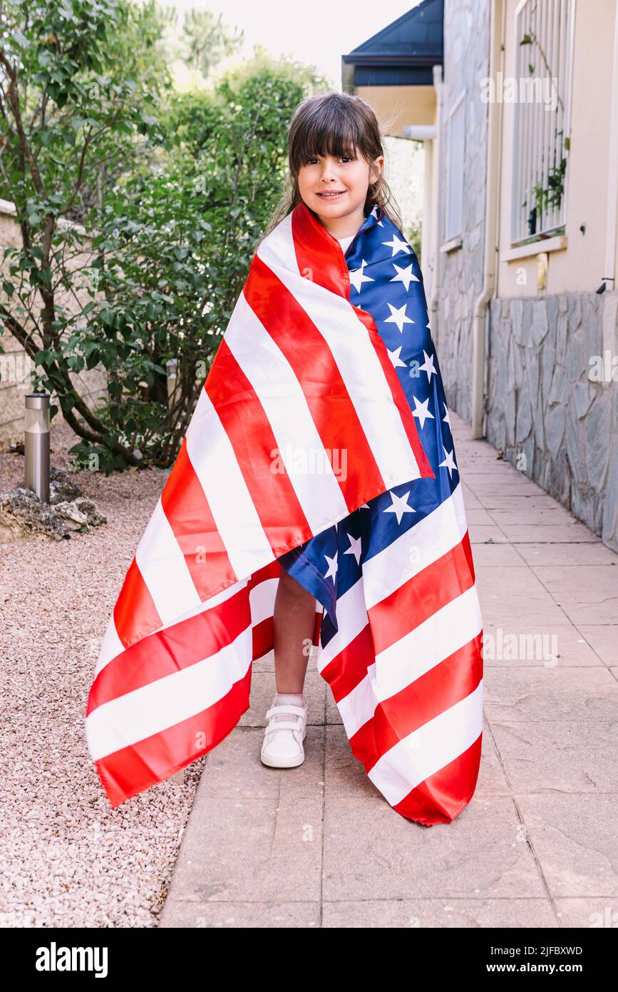 Ragazza dai capelli neri coperta da una grande bandiera americana, nel giardino della sua casa. Concetto di celebrazione, giorno di indipendenza, Stati Uniti d'America, Foto Stock