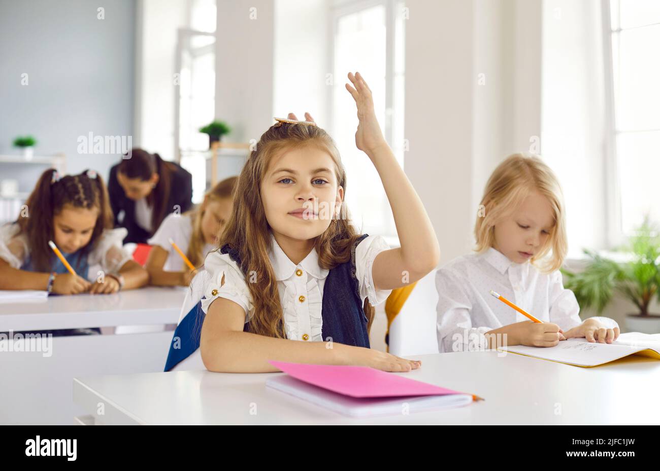 Ritratto di studente di scuola elementare seduto alla scrivania in aula e alzandosi di mano Foto Stock