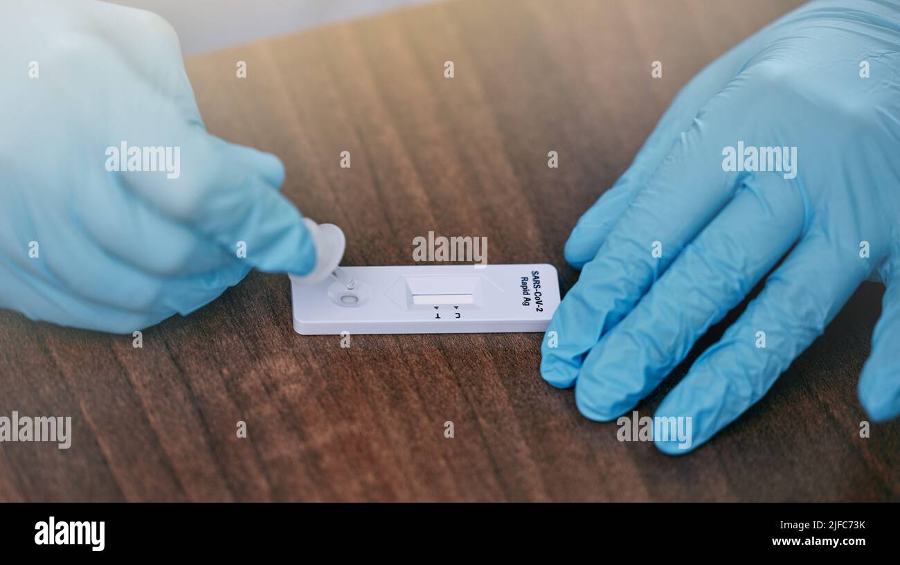 Medico irriconoscibile che indossa guanti e prepara un test covid su un tavolo mentre lavora in un ospedale. Primo piano di un gp irriconoscibile che lavora su un Foto Stock