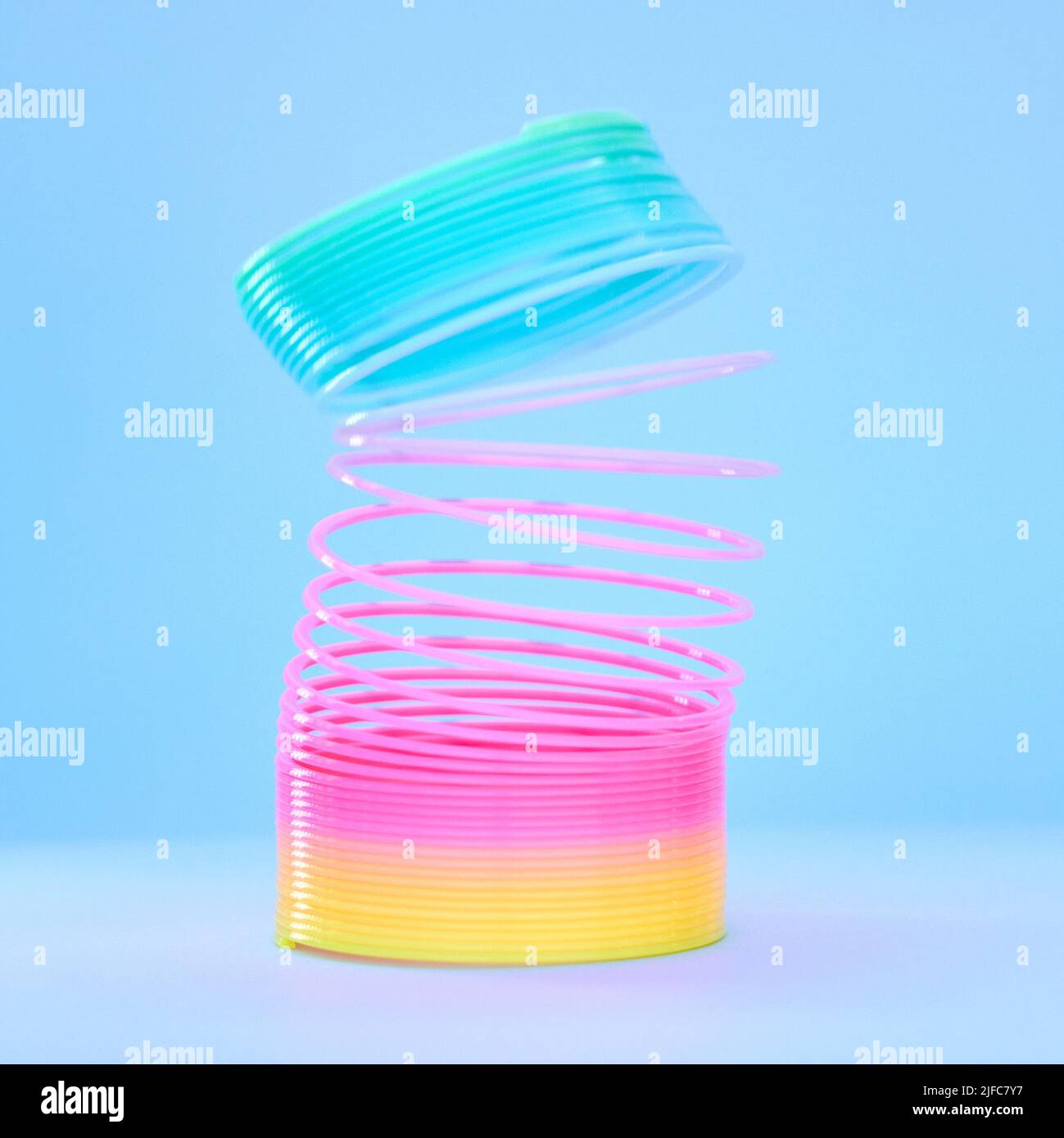 Primo piano di un colorato giocattolo flessibile in plastica arcobaleno slinky in movimento teso isolato su uno sfondo blu. Colori divertenti per l'infanzia Foto Stock