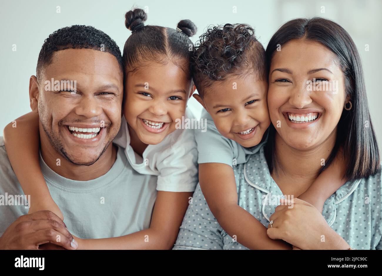 Ritratto di una giovane e felice famiglia mista gara con due bambini che indossano pigiami e seduti a casa insieme. Carino ragazza e ragazzo abbracciando loro Foto Stock