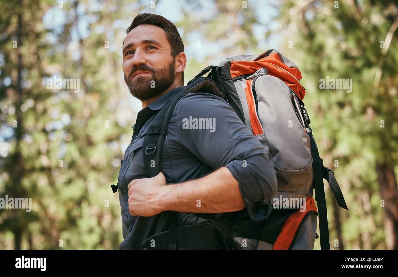 Un uomo caucasico maturo felice che porta uno zaino e trekking da solo nei boschi durante il giorno. Fit e maschio attivo godendo di un trekking, esercizio e. Foto Stock