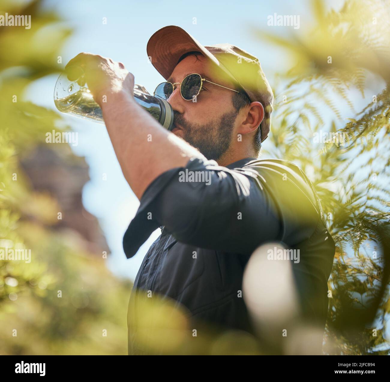 Un uomo caucasico maturo che fa una pausa per bere acqua mentre si fa escursioni da solo nei boschi. Un maschio in forma e attivo che ha sete durante un'escursione durante l'esplorazione Foto Stock