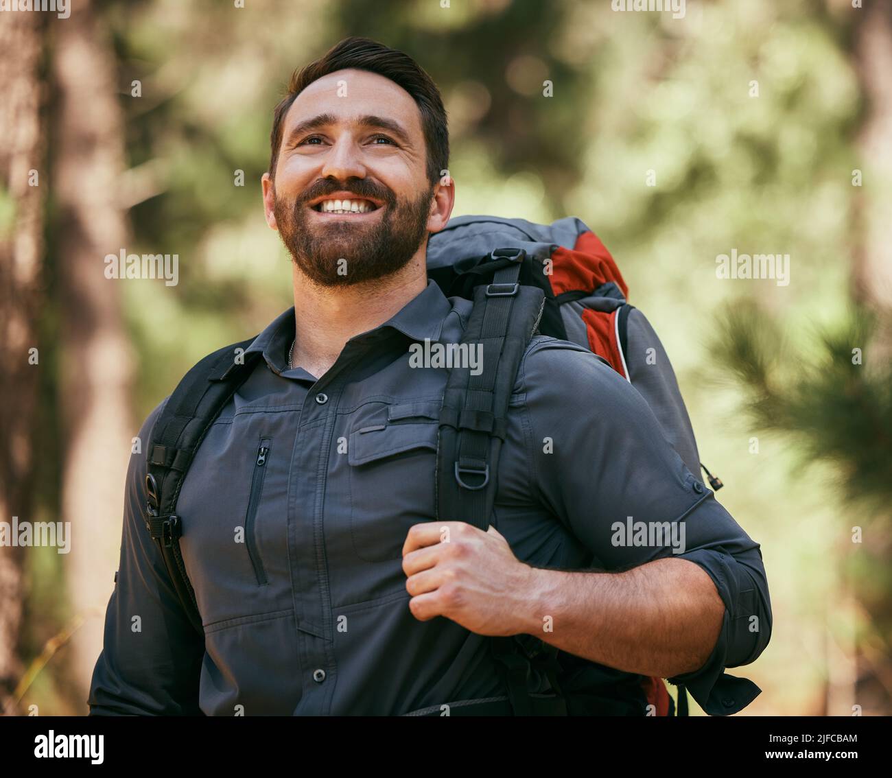 Un uomo caucasico maturo felice che porta uno zaino e trekking da solo nei boschi durante il giorno. Sorridente e uomo attivo godendo la natura mentre Foto Stock