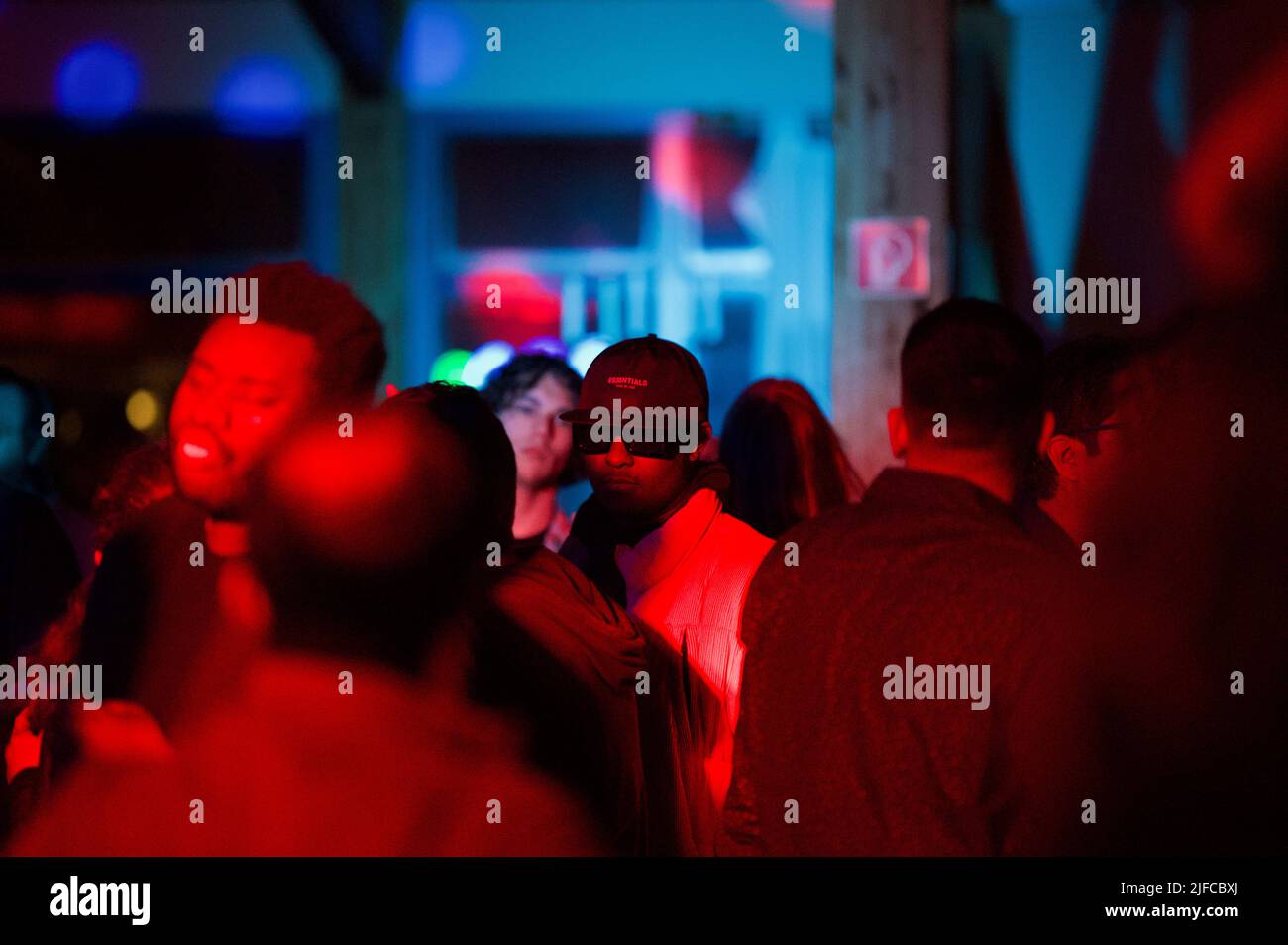 Una persona che guarda una fotocamera dalla folla sotto la luce rossa Foto Stock