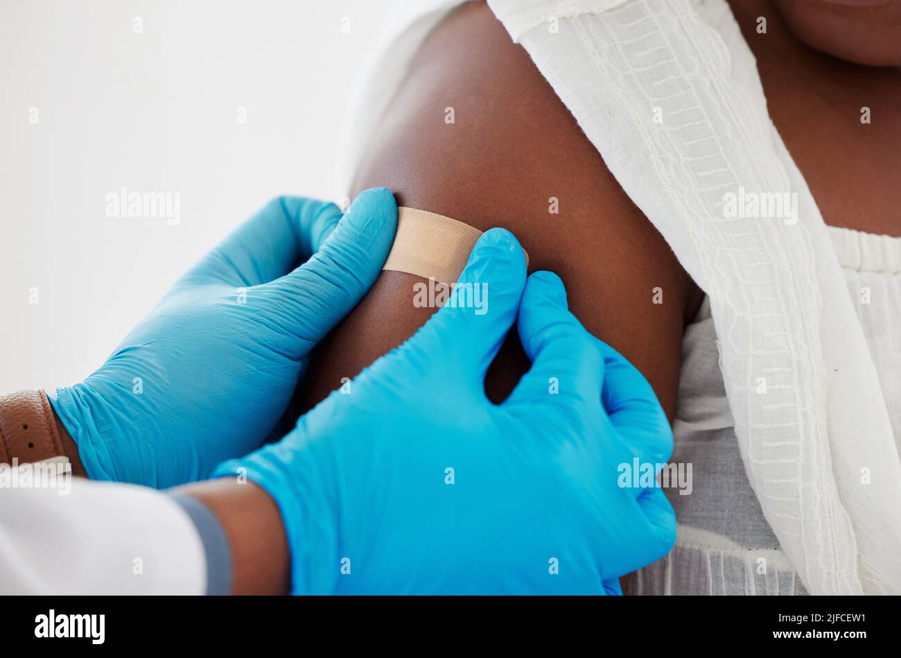 Mano di un medico che applica un cerotto ad un braccio del paziente. Primo piano di un medico che applica un cerotto su un paziente. Paziente afroamericano curato Foto Stock