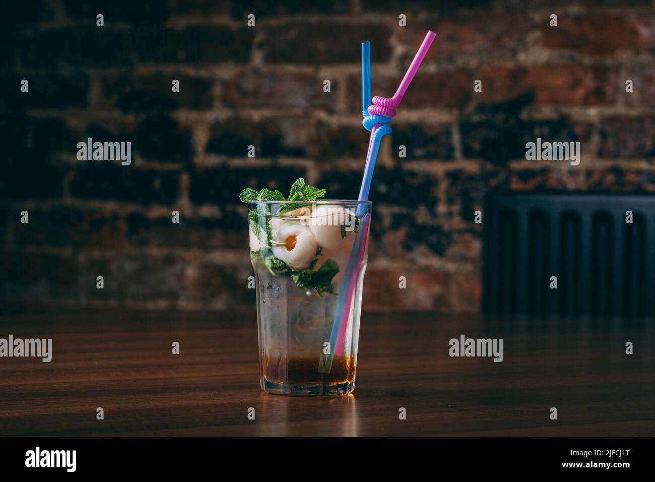 Un primo piano di un cocktail con menta e lychee in un bicchiere con paillette su un tavolo di legno Foto Stock