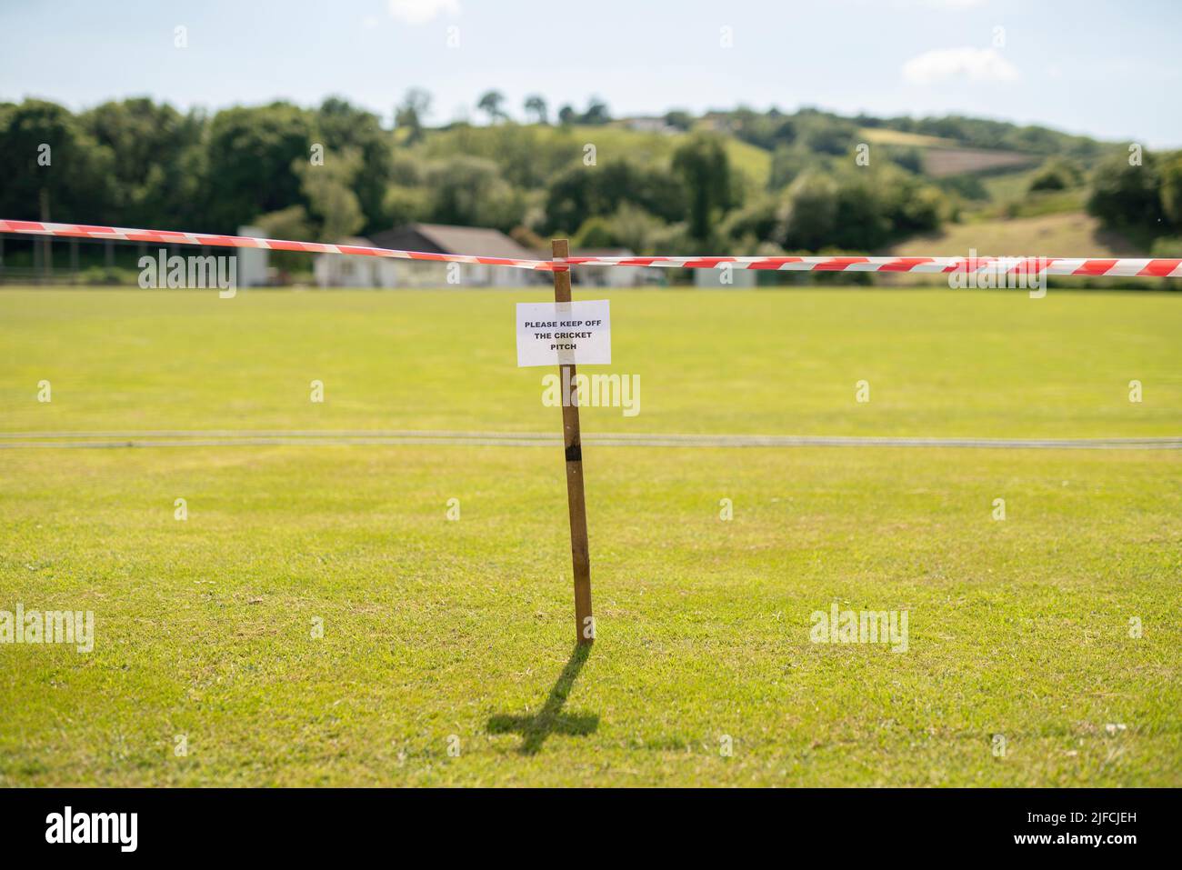 Un cartello con la scritta "si prega di tenere fuori dal campo da cricket" con nastro di avvertimento in un villaggio rurale. Foto Stock