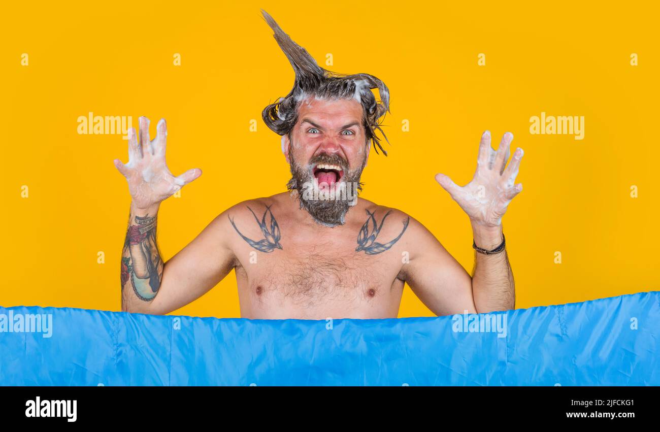 Uomo divertente con schiuma sulla testa facendo la doccia. Ragazzo bearded che lava in bagno. Foto Stock