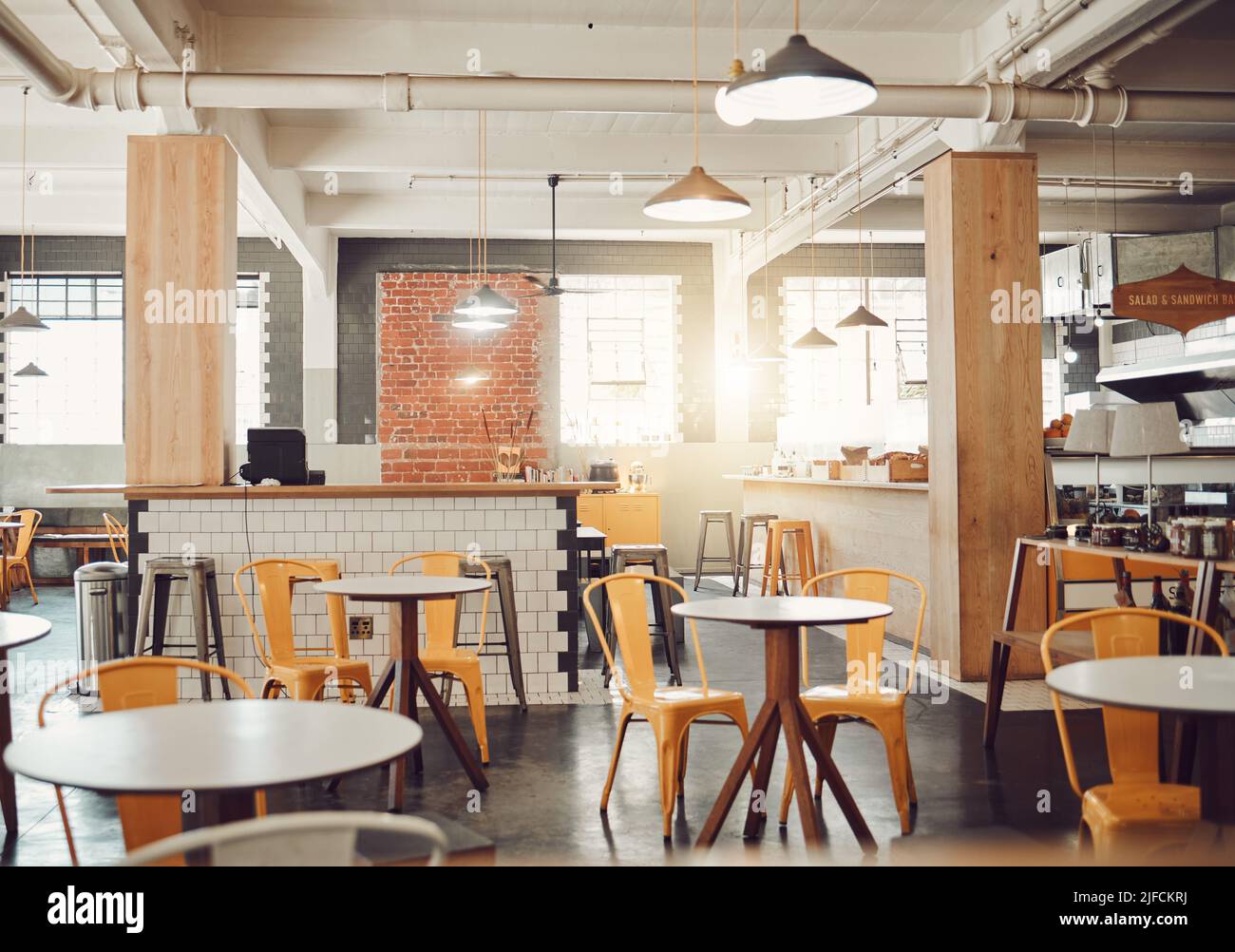 Interno di un moderno caffè vuoto o ristorante durante il giorno. Tavoli rotondi e sedie gialle in un caffè rustico. Caffetteria open space con tubi a vista Foto Stock