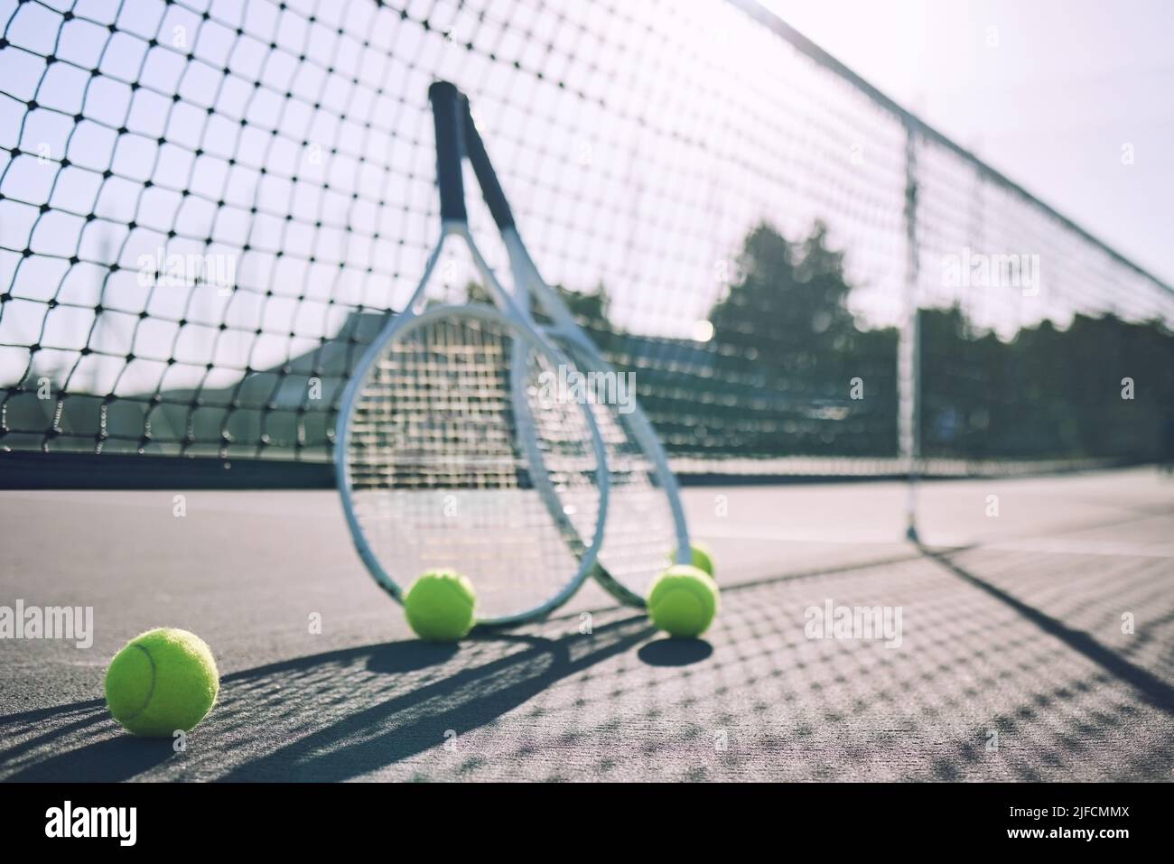 Gruppo di palle da tennis e racchette contro una rete su un campo vuoto in un club sportivo durante il giorno. Giocare a tennis è esercizio fisico, promuove la salute Foto Stock