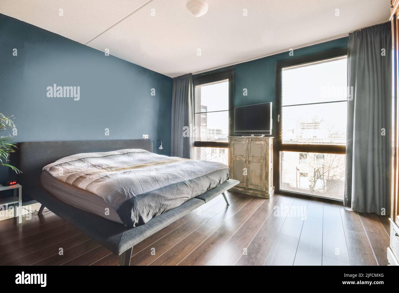 Comodo letto situato vicino alla finestra con tenda nella camera da letto luminosa di appartamento contemporaneo Foto Stock