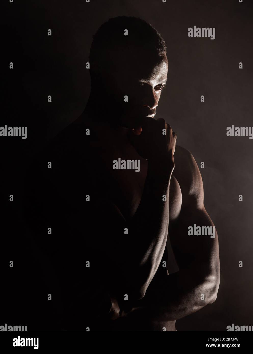 Un bel giovane afroamericano muscoloso in studio su sfondo scuro. Un atleta maschile macho che guarda pensieroso isolato su nero Foto Stock