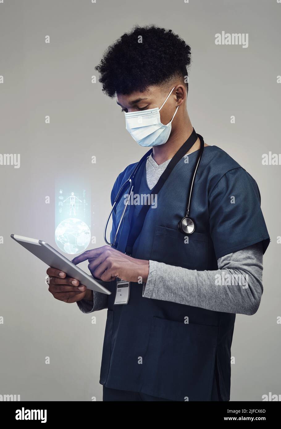 Indossare la maschera, il suo bene per i numeri. Shot di un infermiere di sesso maschile che tiene un tablet digitale in piedi su uno sfondo grigio. Foto Stock