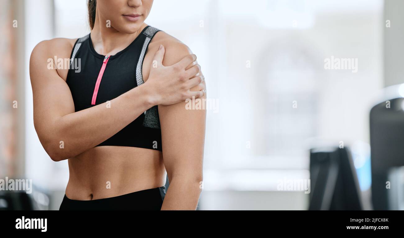 Istruttore sconosciuto da solo in palestra e che soffre di lesioni alle spalle. Un allenatore in piedi e braccio di strofinamento durante l'allenamento nel centro fitness. Una donna Foto Stock