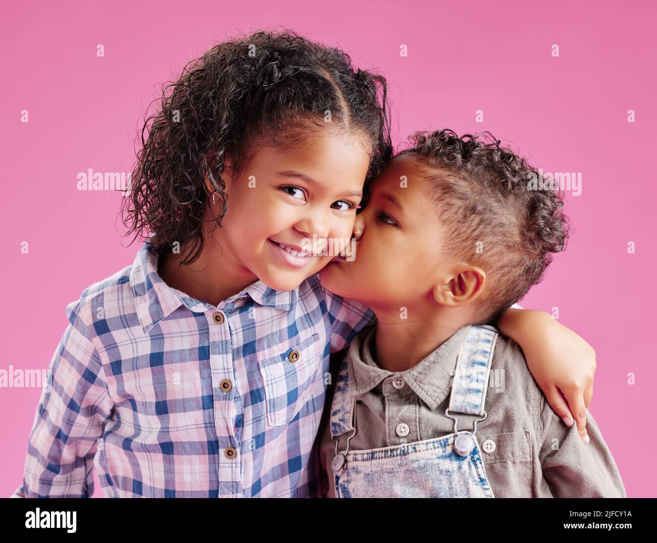 Due bambini solo in posa ed essendo affettuoso su uno sfondo rosa copyspace. I fratelli di razza mista afro-americana baciano mentre si legano in un Foto Stock