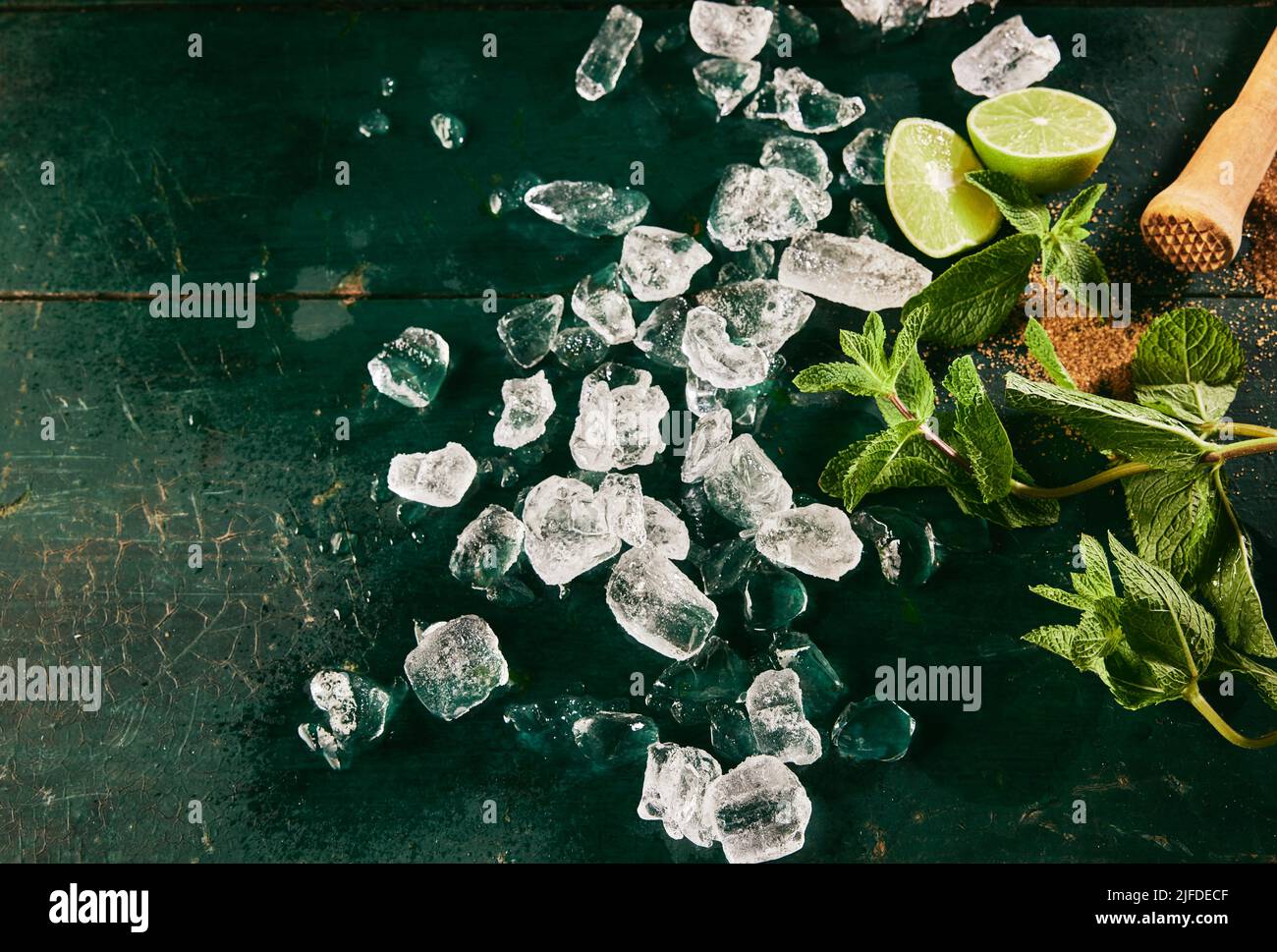 Vista dall'alto degli ingredienti per il cocktail mojito, tra cui un mucchio di cubetti di ghiaccio sparsi su un tavolo shabby con foglie di menta verde e fette di lime fresche Foto Stock