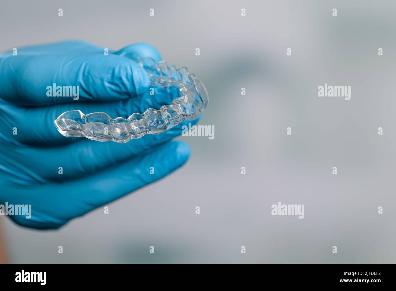 Mano dentista in guanti blu che presentano un allineatore trasparente rimovibile di fronte alla sala odontoiatria Foto Stock