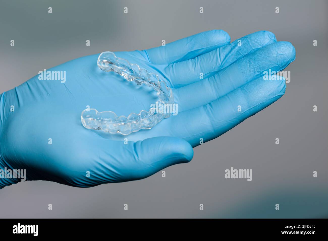 Mano dentista in guanti blu che presentano un allineatore trasparente rimovibile di fronte alla sala odontoiatria Foto Stock