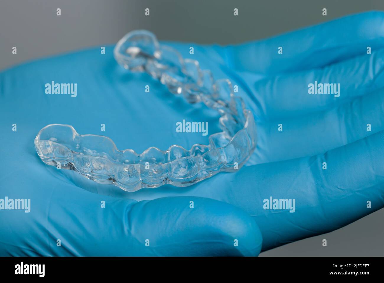 Mano dentista in guanti blu che presentano un allineatore trasparente rimovibile di fronte alla sala odontoiatria Foto Stock