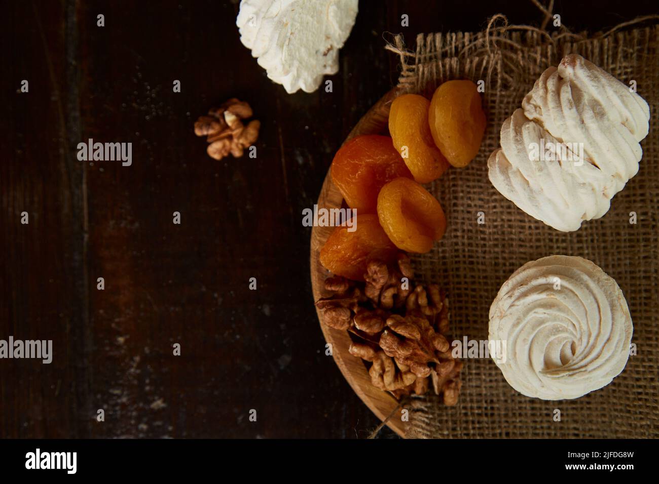 Marshmallow naturale con albicocche secche, noci su piatto di legno sotto la luce del sole e una tazza di tè. Sfondo rustico. Giardino accogliente. Spazio di copia. Foto Stock