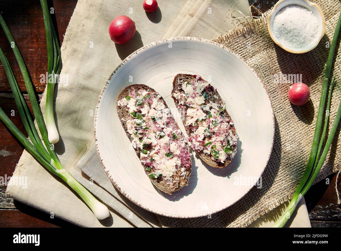 Spalmatura di un ravanello sano su pane di pasta madre. Toast al burro di rafano. Mangiare fuori. Rustico cibo piatto laici. Antipasto sano, pane naturale di pasta naturale con striscio di rafano e cipolla giovane primavera sotto l'ombra. Foto Stock