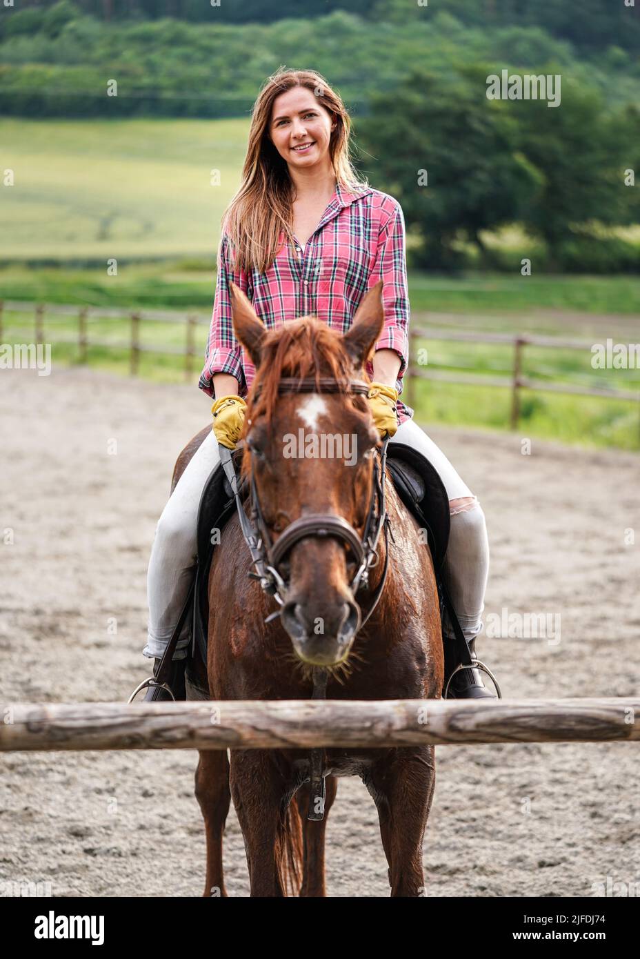 Giovane donna in camicia che riposa sul cavallo marrone - il cappotto bagnato dal sudore - dopo aver cavalcato, sorridente Foto Stock