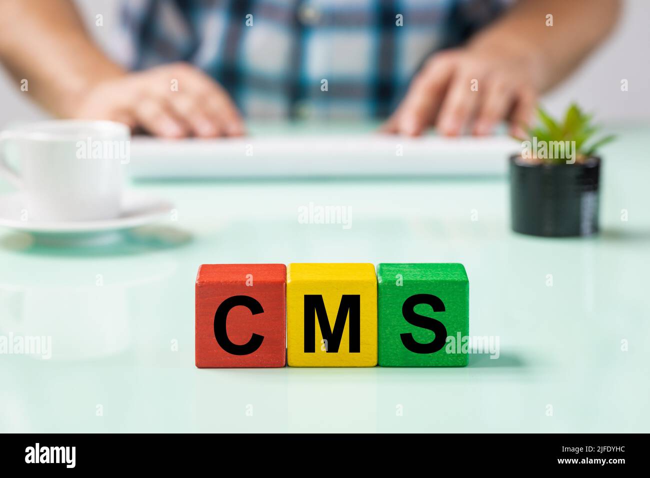 Un impiegato dietro una scrivania ad un calcolatore, blocchi di legno, CMS di abbreviazione, sistema di gestione di contenuto, software, utilizzato per pubblicare contenuti su siti web, mo Foto Stock