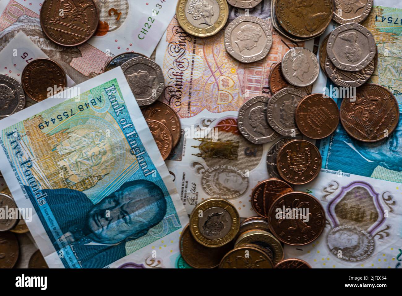 Le banconote e le monete in sterline bristish si diffondono in modo casuale, perdendo valore a causa dell'inflazione, tagli fiscali Foto Stock